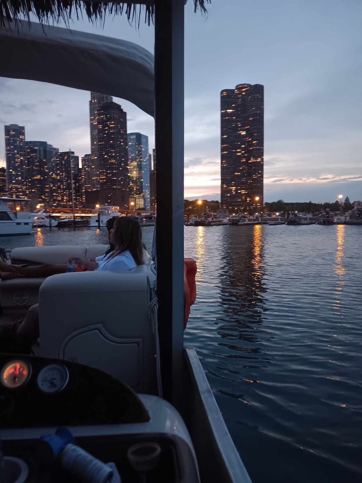 Looking out from the boat at dusk, a guest seated by the rail and downtown towers lit up across the water