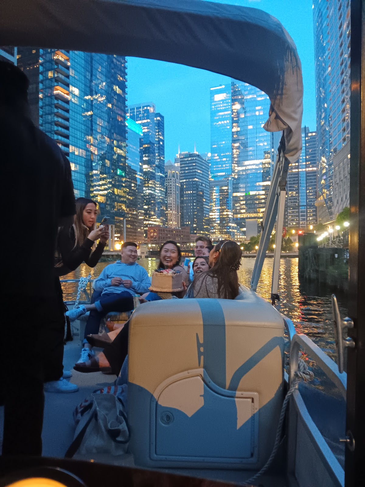 Guests on the boat at night with glowing skyscrapers rising behind the canopy